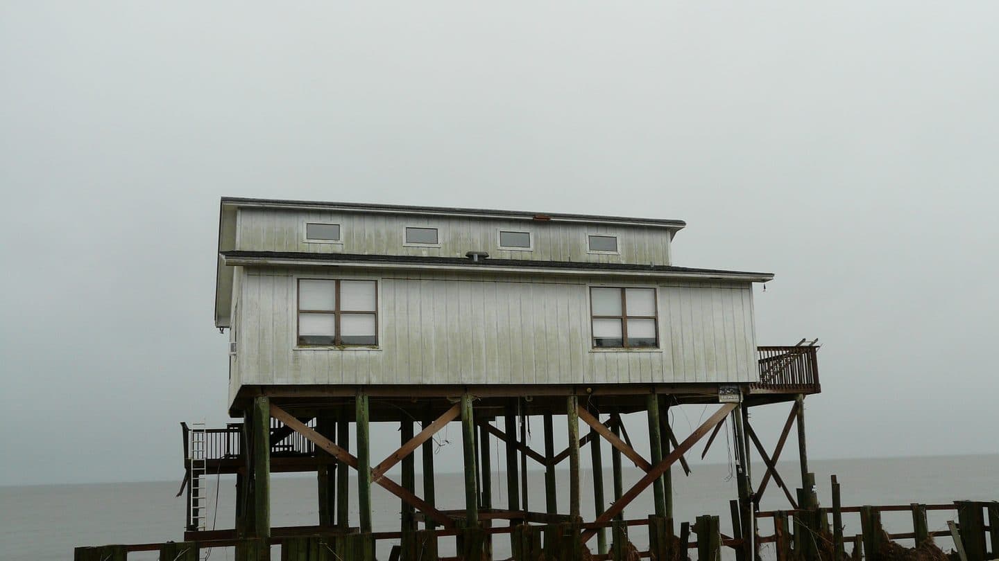 Weathered stilt house sitting empty at the water's edge with stained siding
