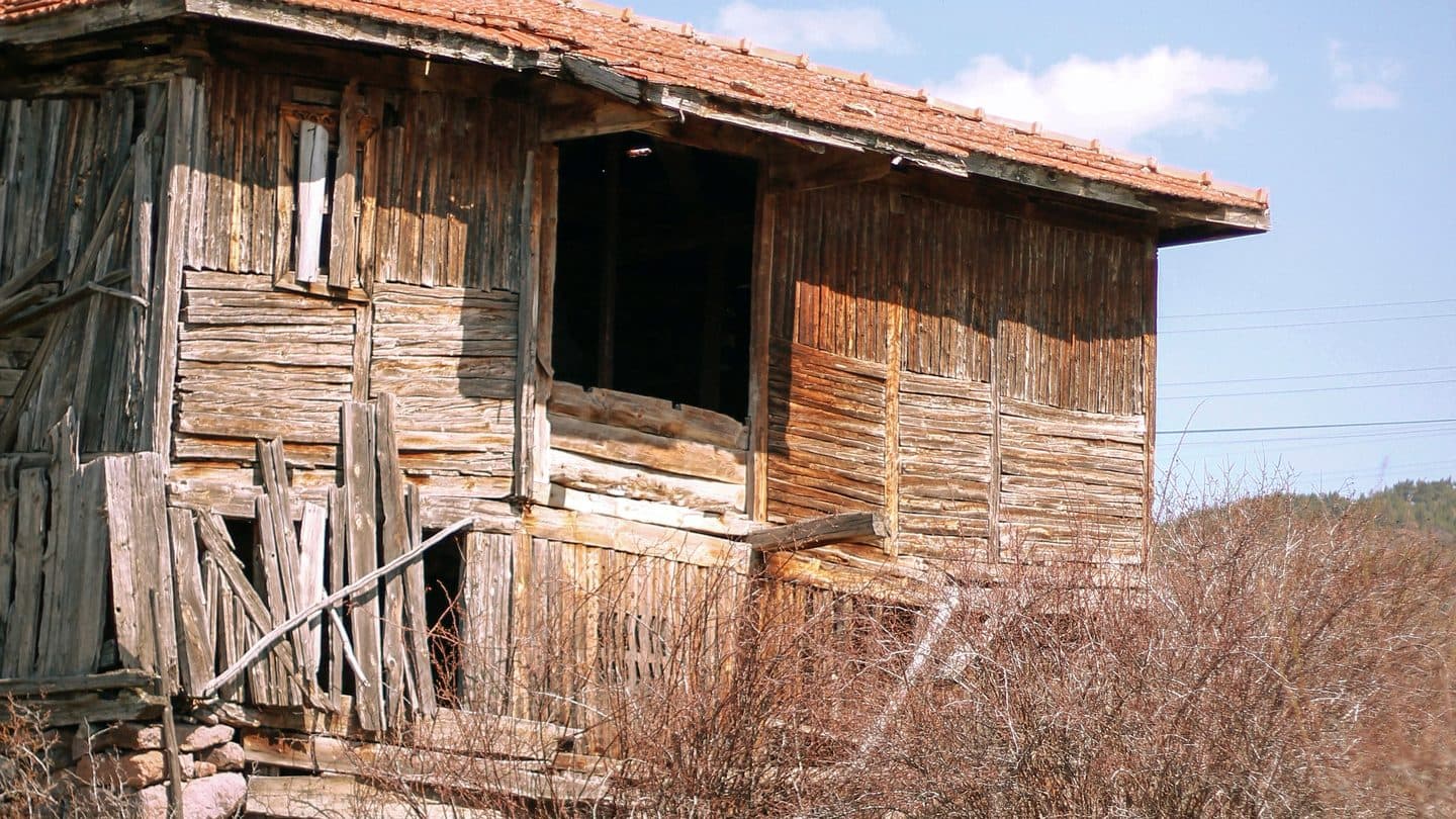 Ruined wooden house with missing planks, a crumbling stone base, and rubble in front