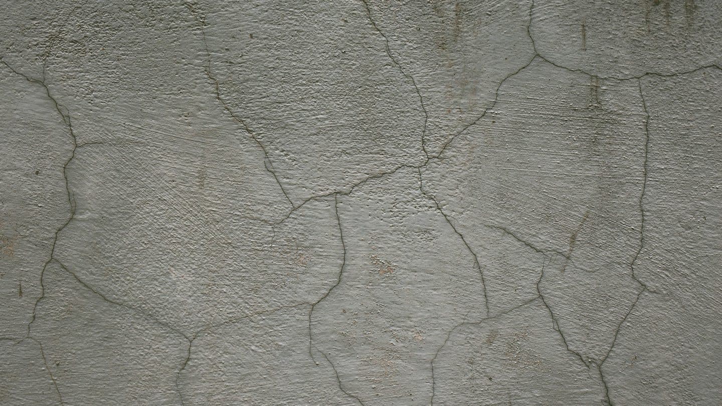 Close-up of a cracked gray plaster and concrete wall typical of a settled foundation