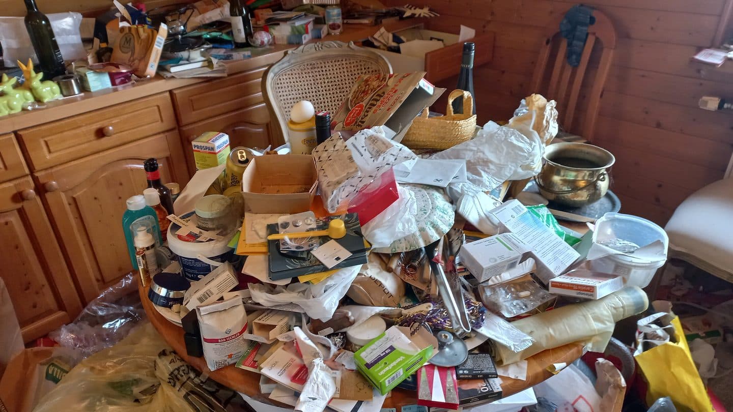 Dining table buried under papers, bottles, and bags in a hoarded house