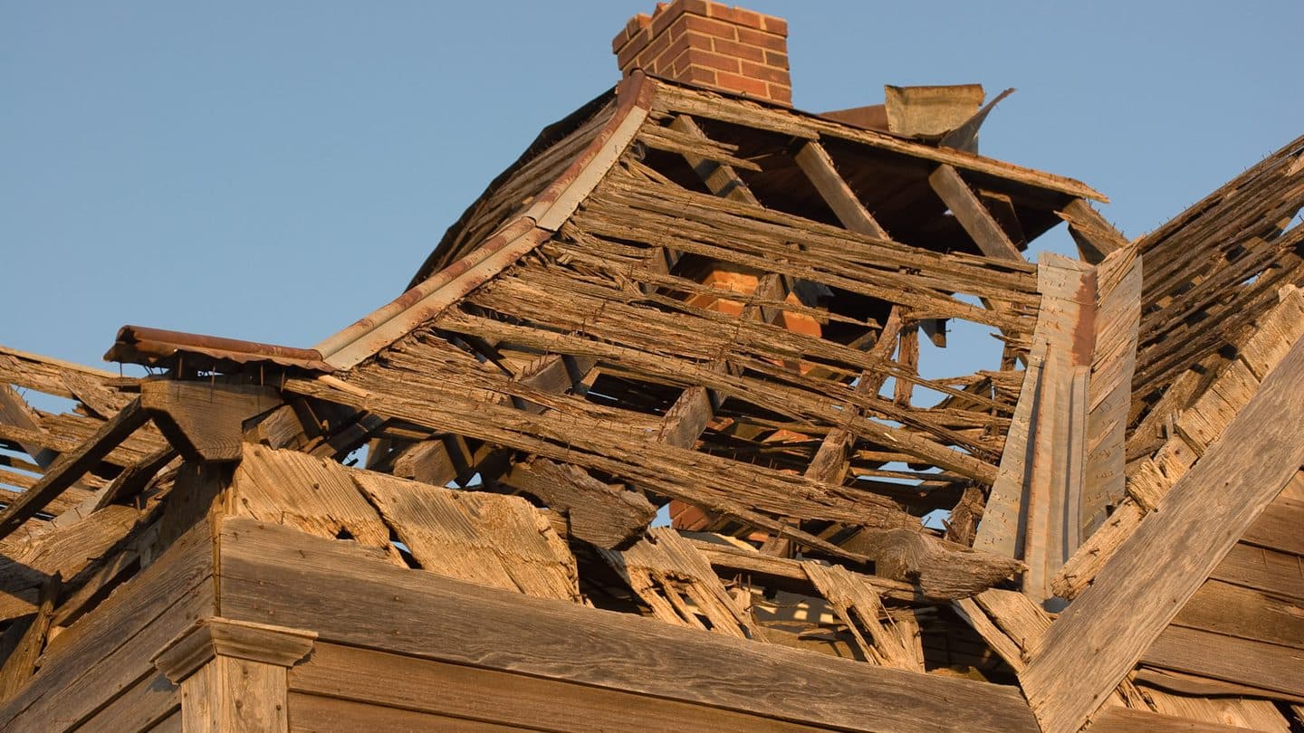 Close-up of a failed wooden roof with broken rafters around a brick chimney