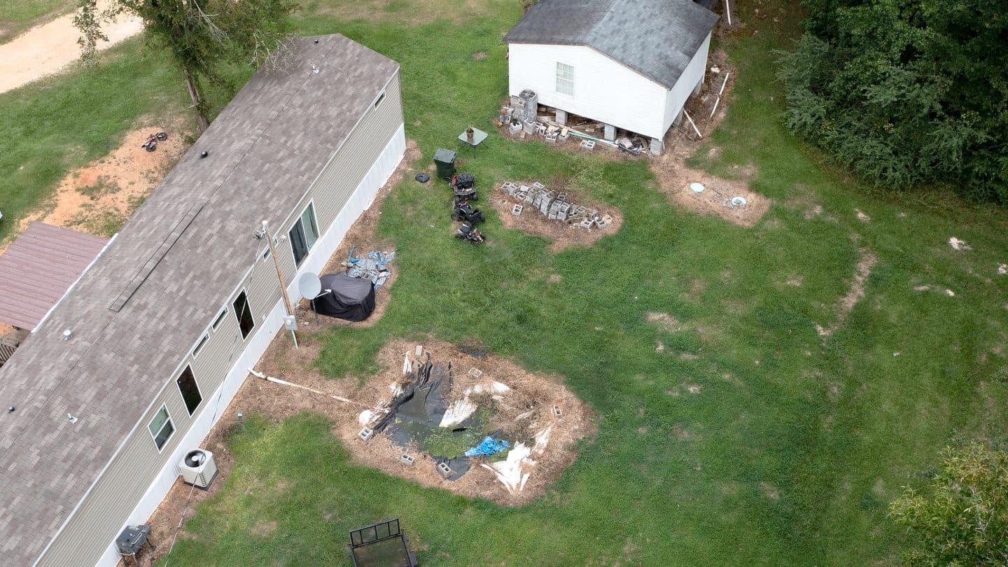 Yard showing septic tank lids and an open drain field pit next to the house