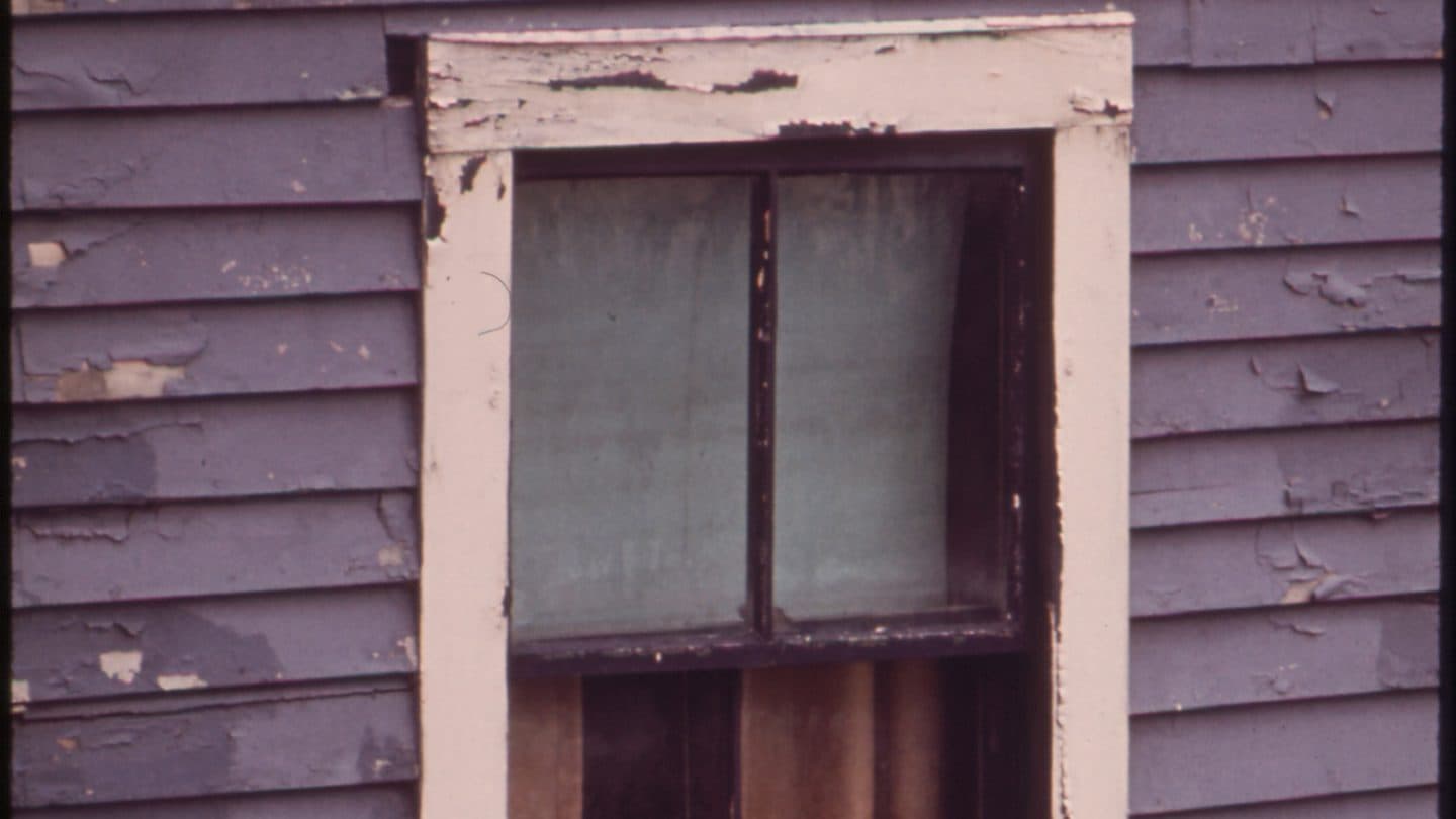 Peeling clapboard siding on a lived-in house that has gone without exterior upkeep