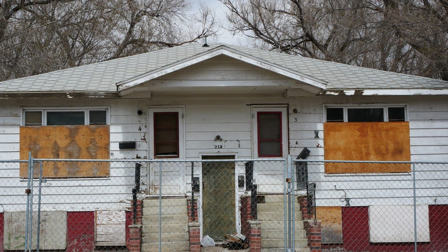 Boarded-up house behind a chain-link fence, closed to keep people out