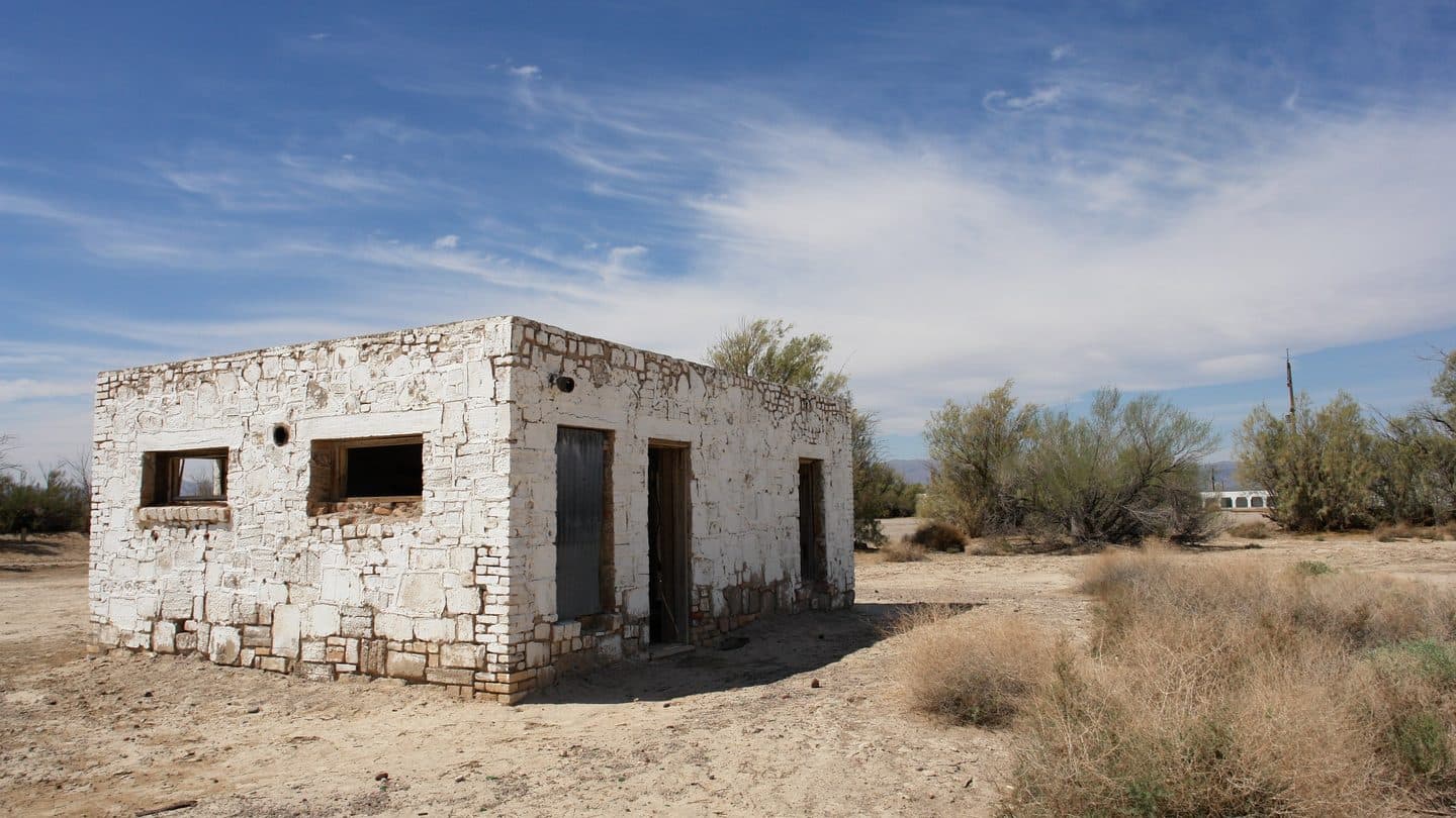 Abandoned masonry house with empty door and window openings in dry grass