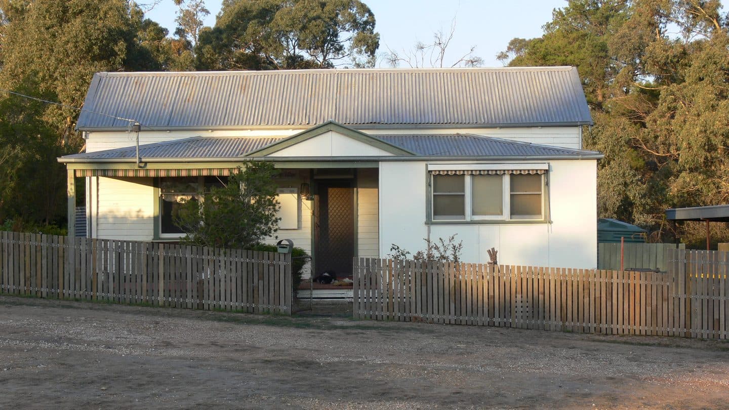 Older cottage with asbestos cement sheeting on the front wall and a weathered porch